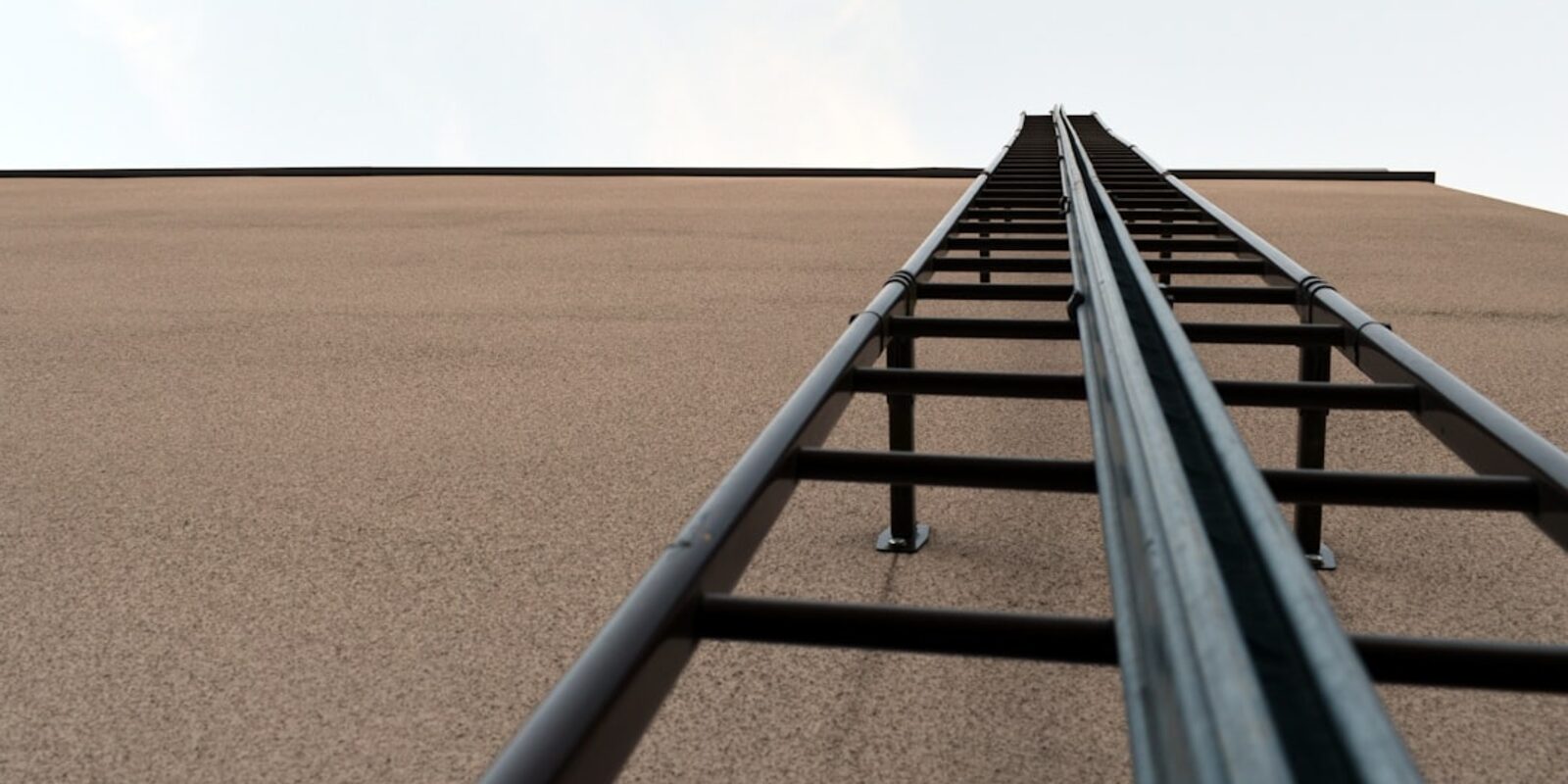 Fixed metal access ladder mounted against a beige wall, viewed from below
